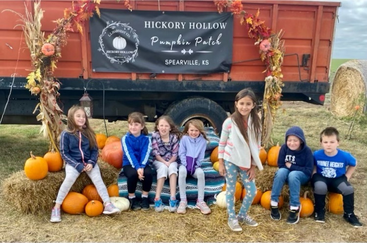 kids on hay bales in front of sign on a truck that says Hickory Hollow Pumpkin Patch